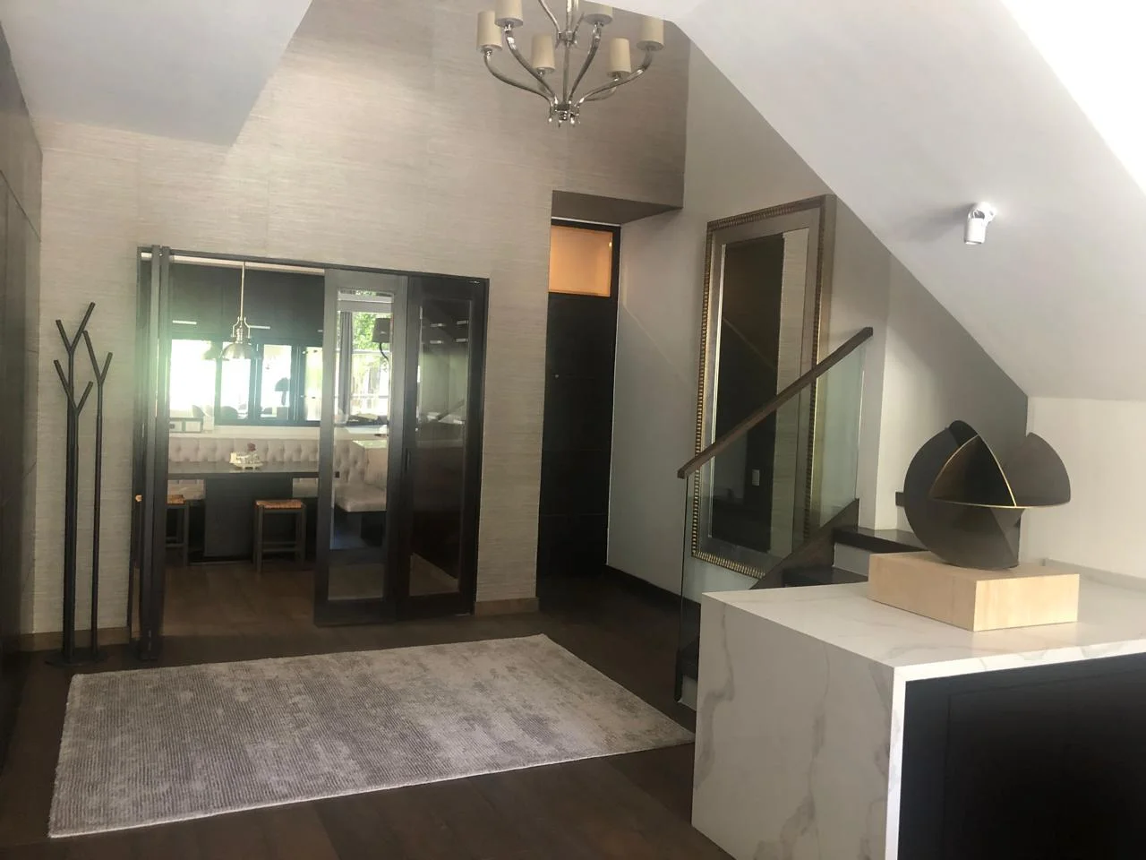 Vestíbulo residencial con escalera, consola de mármol y escultura